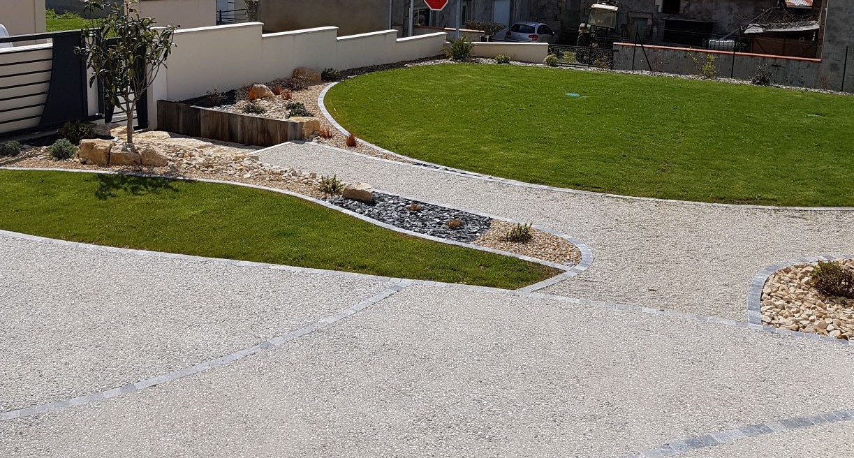 Allée d'entrée de pavillon structurée et gravillonnée avec espace pelouse et massif rocailleux